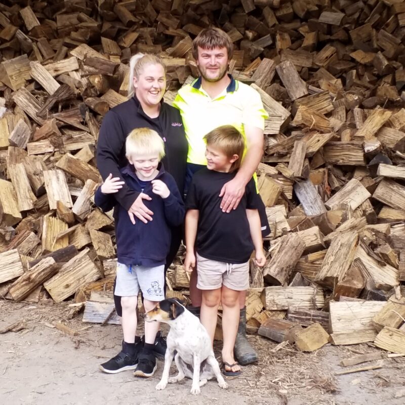 Image of Ben, Jenna, Corban, Lukah and Mika the dog standing in front of a large pile of chopped blue gum firewood